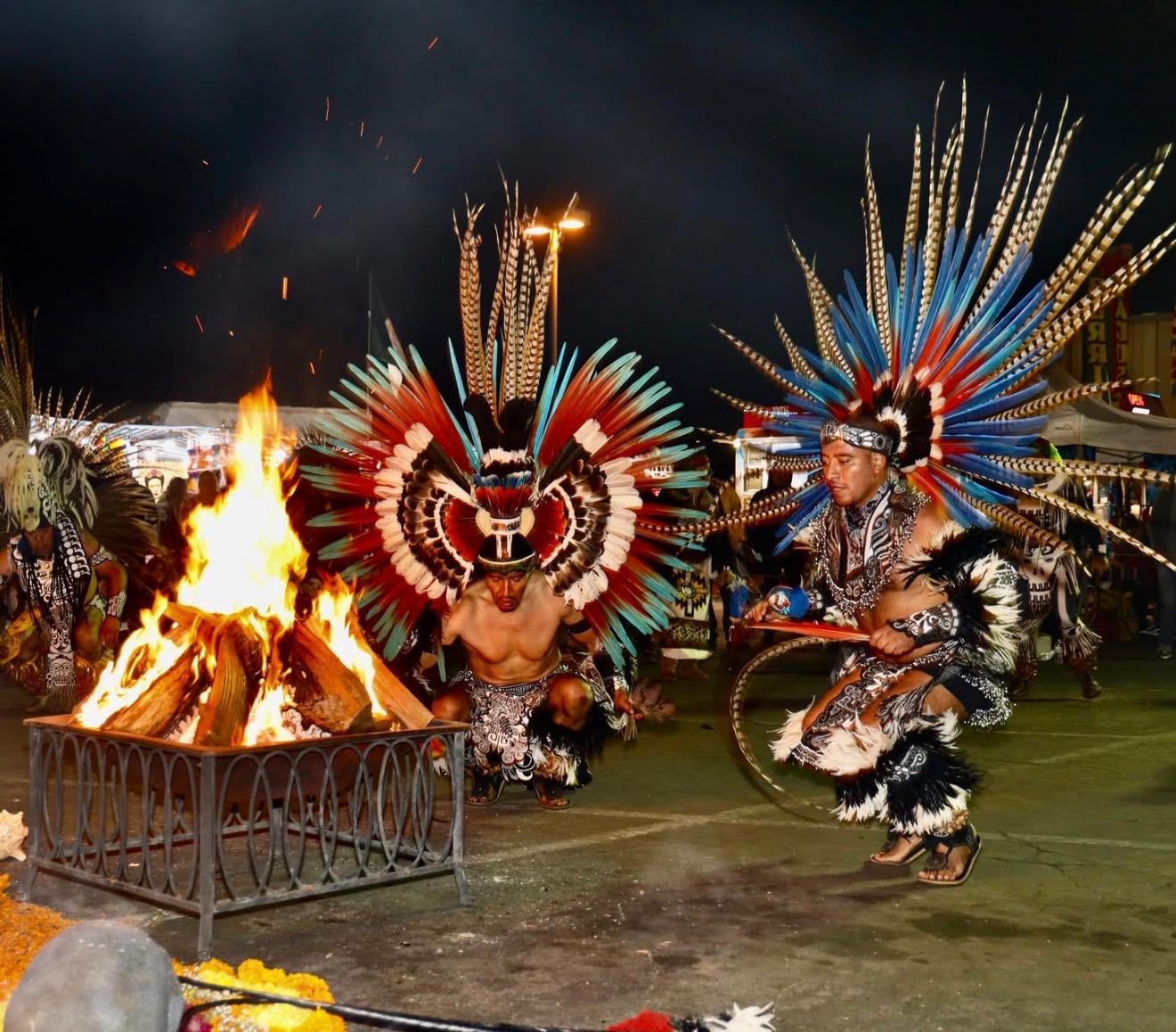 Two Aztec dancers performing around a ceremonial fire at night